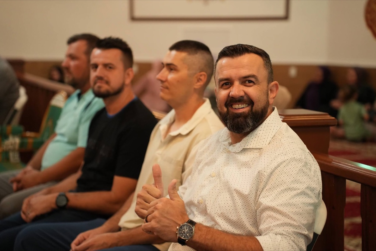 Smiling men of the džemat seated at an event, one giving a thumbs up