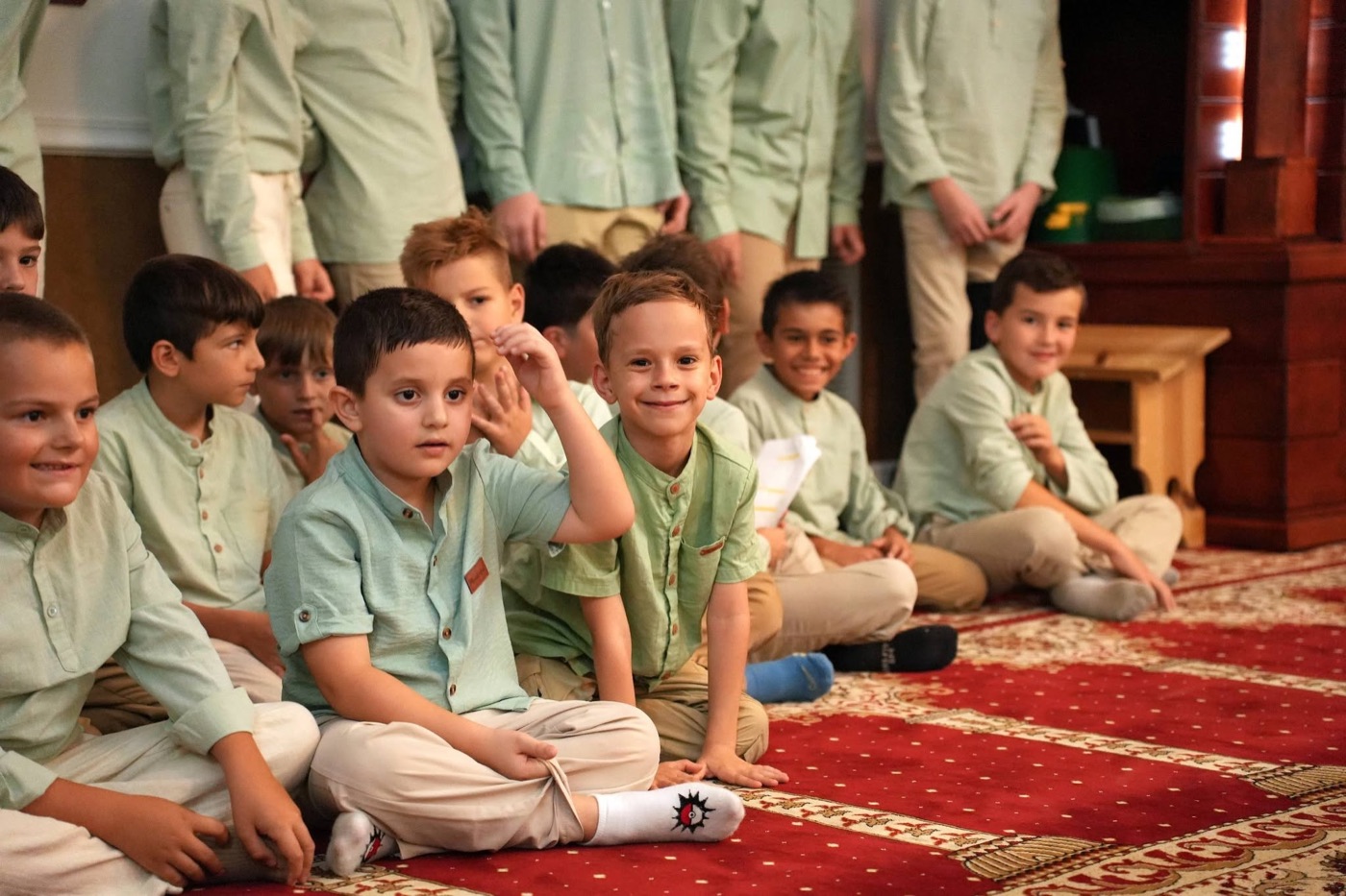 Smiling mekteb boys in matching outfits seated on the mosque carpet