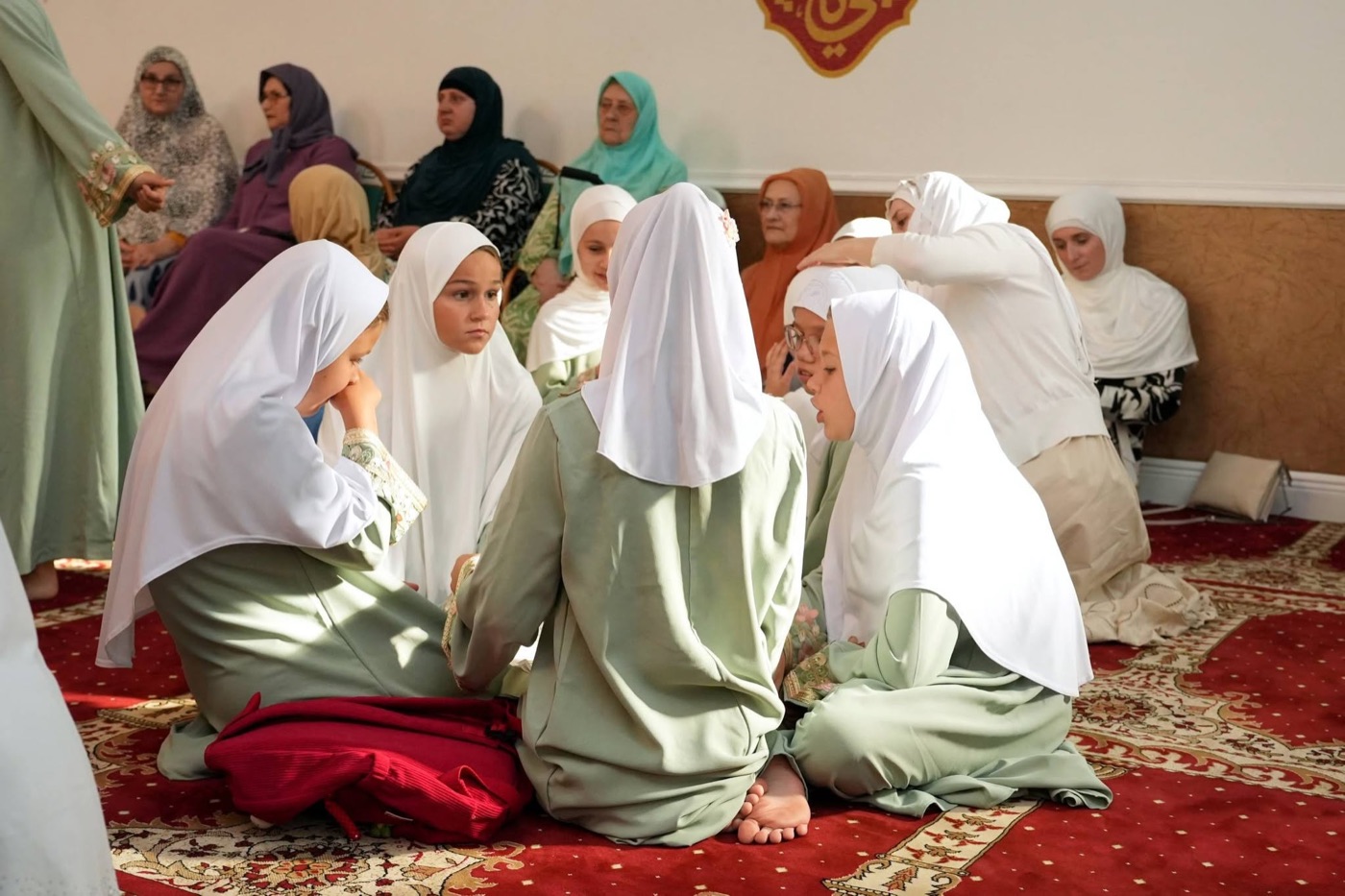 Mekteb girls in white hijabs seated together, with women of the džemat behind them